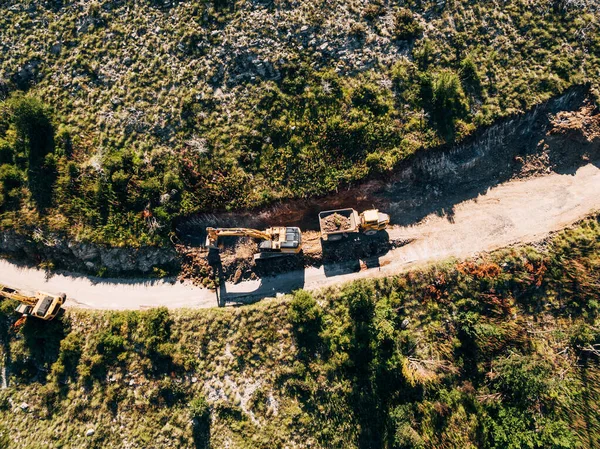 Yellow tracked tractor loads a quarry vehicle with sand. View from above