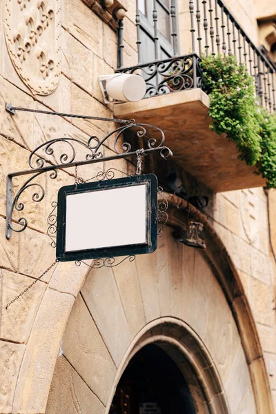 Krásný prázdný nápis v kovaném kovovém rámu visí na kamenné zdi budovy na pozadí balkónu a zeleně — Stock fotografie
