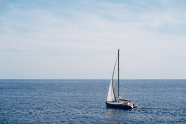 Rüzgarda dalgalanan beyaz yelkenli küçük bir tekne Denizde yelken açar