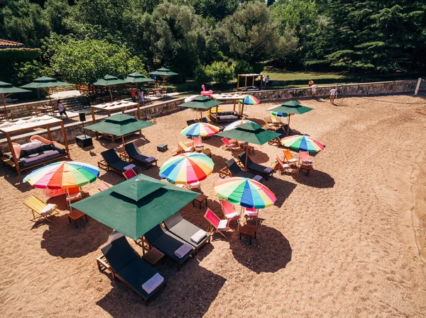 Espreguiçadeiras sob guarda-sóis coloridos na praia contra o pano de fundo de montanhas verdes — Fotografia de Stock