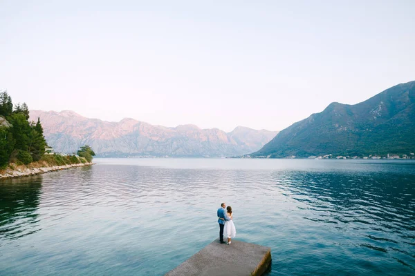 Époux étreinte mariée debout sur la jetée sur le fond des montagnes et de la mer dans l'après-midi — Photo