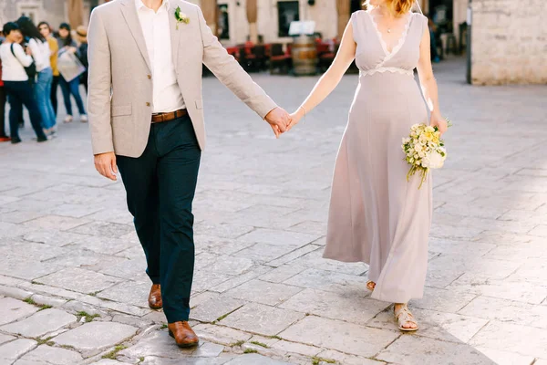 Наречений і наречений тримають руки на бруківці міської площі — стокове фото