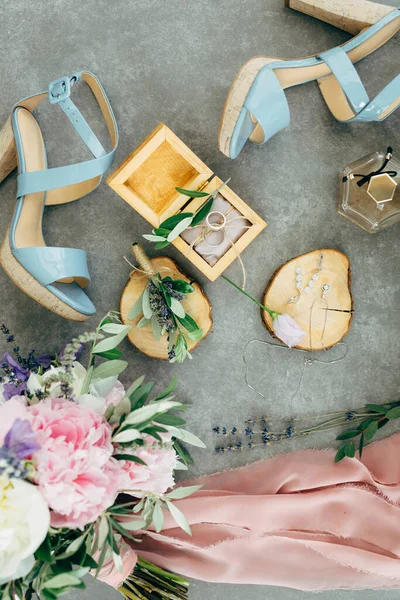 Cincin pernikahan terletak di kotak kayu yang dikelilingi oleh sandal dengan tumit, bunga dan ranting, karangan bunga dan syal di lantai — Stok Foto