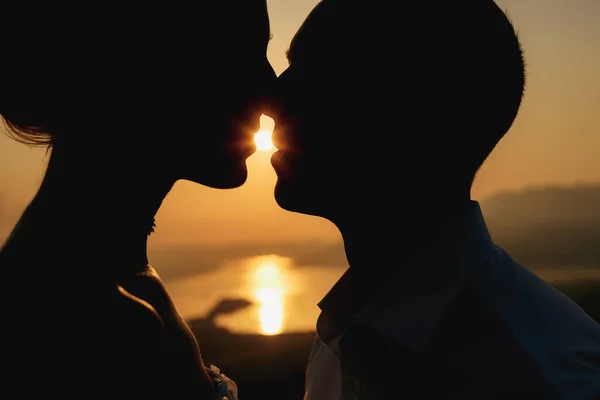 Siluetas de un hombre y una mujer besándose al atardecer sobre el fondo del mar, primer plano —  Fotos de Stock