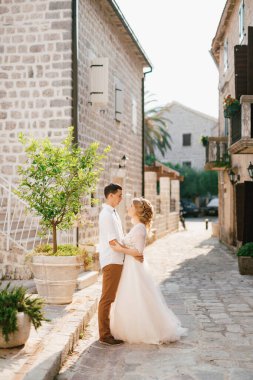 Gelin ve damat, eski Perast kasabasının güzel ve rahat bir sokağında genç bir ağacın yanında sarılıyorlar. 