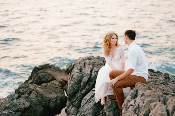 A noiva e sentar-se e conversar sobre as rochas junto ao mar e olhar um para o outro — Fotografia de Stock