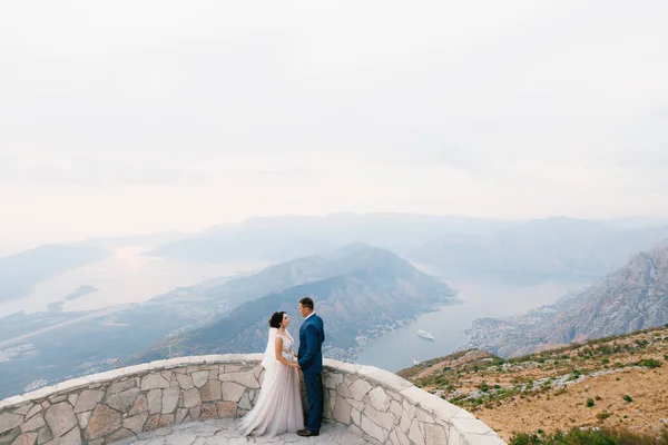 De bruid en bruidegom staan hand in hand op het observatiedek op de berg Lovcen met uitzicht op de baai van Kotor, bovenaanzicht — Stockfoto