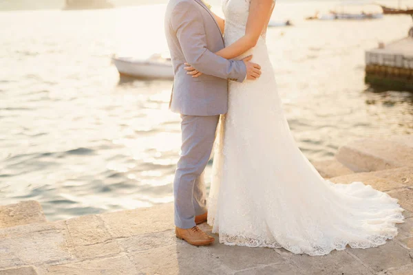 Braut und Bräutigam umarmen sich an einem sonnigen Tag auf dem Steg am Wasser, hinter ihnen schwimmt ein weißes Boot — Stockfoto