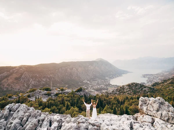 Les mariés se tiennent debout sur le mont Lovcen les mains en l'air et regardent la baie de Kotor — Photo