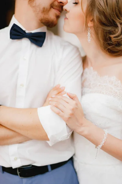 De bruidegom vouwde zijn armen over zijn borst, de bruid omhelst hem zachtjes bij de elleboog en staat op het punt te kussen, close-up — Stockfoto