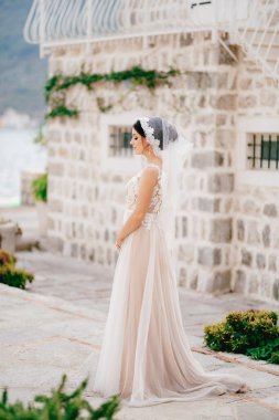 Dantel peçeli nazik bir gelin eski Perast kasabasında beyaz tuğladan bir evin yanında duruyor. 