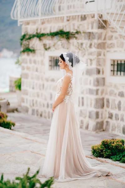 Seorang pengantin yang lembut dengan kerudung renda berdiri di dekat rumah bata putih di kota tua Perast — Stok Foto