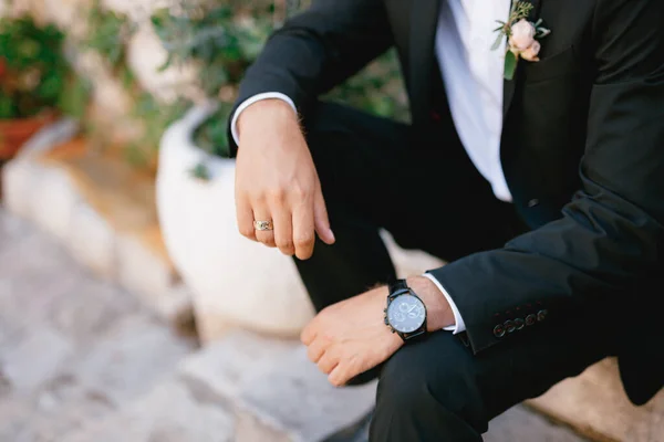 Un hombre en un traje con un boutonniere y un reloj de pulsera está sentado en un escalón, de cerca —  Fotos de Stock