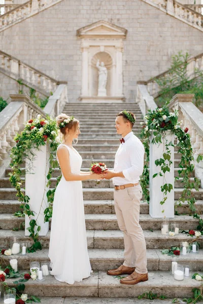 A menyasszony és a vőlegény áll a lépcsőn a Született Szűz Mária templom Prcanj és tartja az esküvői csokor együtt — Stock Fotó
