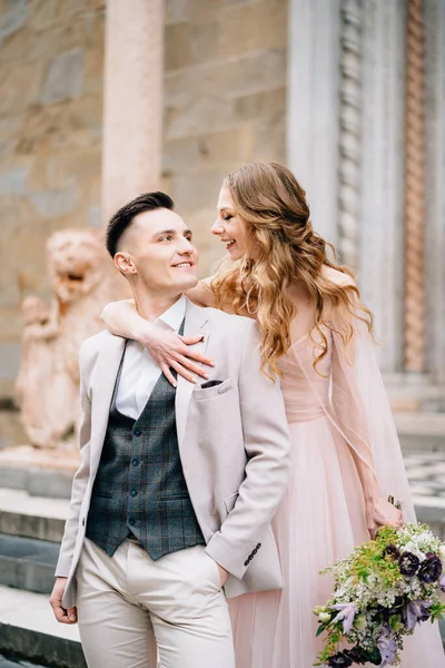 Novia con un ramo de flores abraza hombros de novio sonriente en las escaleras a la entrada de la Basílica de Santa Maria Maggiore. De cerca. —  Fotos de Stock