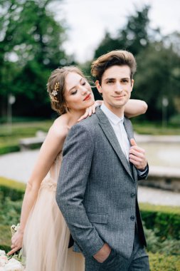 Gelin elini damadın omzuna koydu, arkadan, çeşmenin önünde ona sarıldı. Como Gölü, İtalya. Kapat.