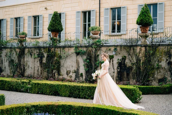 Pengantin dalam gaun merah muda dengan karangan bunga berjalan melalui taman melewati vila tua. Danau Como, Italia — Stok Foto