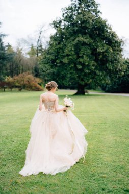 Bir buket çiçekli pembe elbiseli gelin yeşil bir parkta yürüyor. Como Gölü. Arka plan