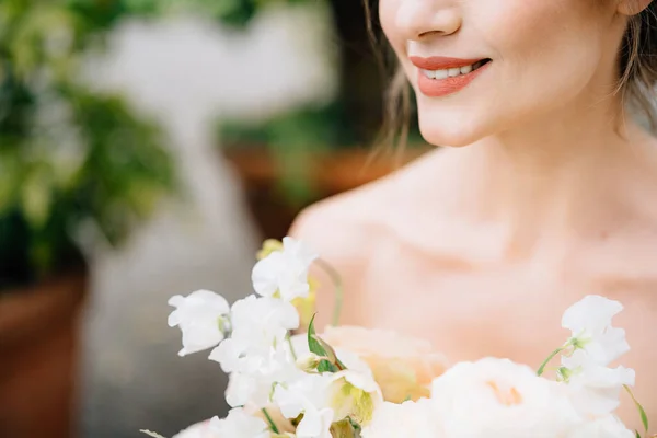 Glimlachende bruid in een prachtige jurk met een boeket bloemen op een achtergrond van een groene boom in een bad — Stockfoto