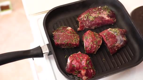 Close-up van een restaurant chef-kok in handschoenen zet steak op een grill pan. Een kok roostert een sappig stuk vlees op een grill pan in een restaurant. — Stockvideo