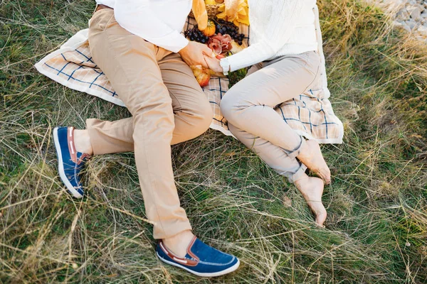 Man och kvinna sitter på en filt och håller hand på gräsmattan. Mannen är skum i gympaskor, och kvinnan är barfota — Stockfoto
