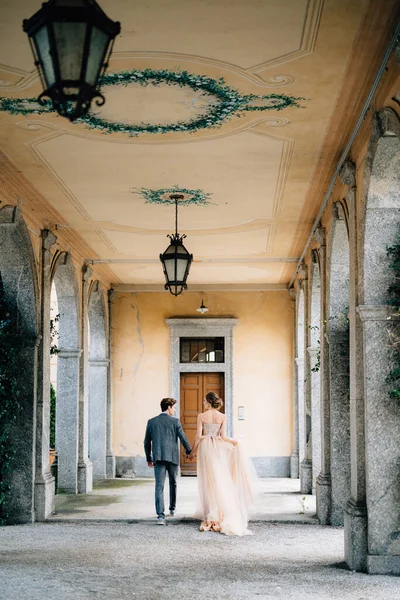 Brud och brudgum gå längs den gamla terrassen med kolumner sammanflätade med grön murgröna. Comosjön, Italien. Bakifrån — Stockfoto