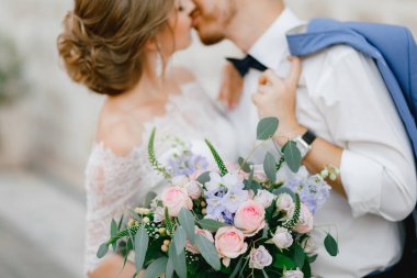 Gelin ve damat, eski Perast kasabasında güzel bir tuğla evin yakınında sarılıp öpüşüyorlar.