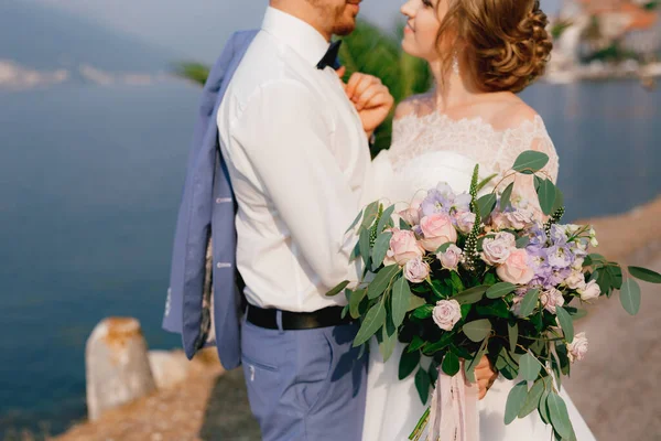 La mariée et le marié s'embrassent sur la jetée, la mariée tient un bouquet dans sa main, gros plan — Photo