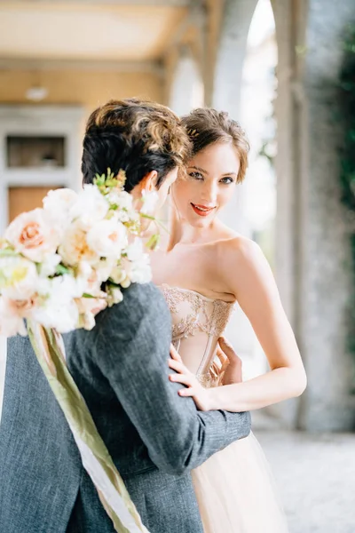 Bräutigam umarmt Braut mit einem Blumenstrauß auf einer alten Terrasse mit Bögen, die von grünem Efeu umschlungen sind. Comer See. Nahaufnahme — Stockfoto