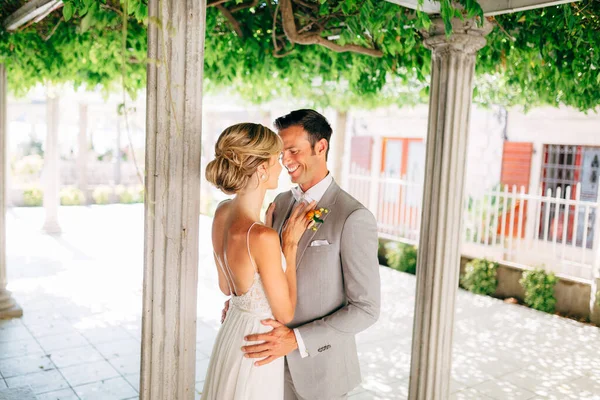 Gli sposi stanno tra le colonne, abbracciati e sorridenti. La sposa mise le mani sul petto degli sposi. — Foto Stock