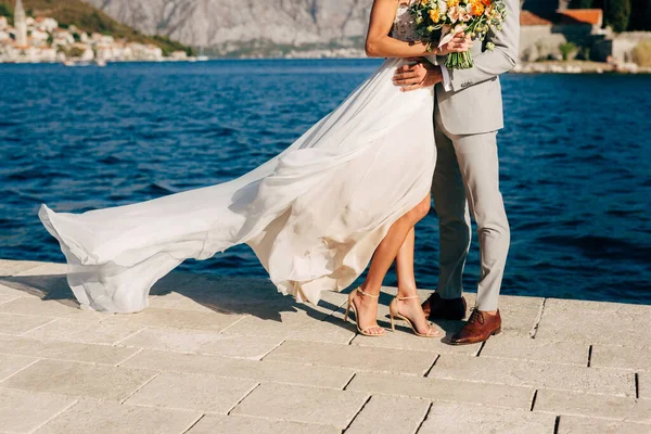 Legs of the bride and groom hugging on the pier in the Bay of Kotor behind them the old town of Perast — Stock Photo, Image