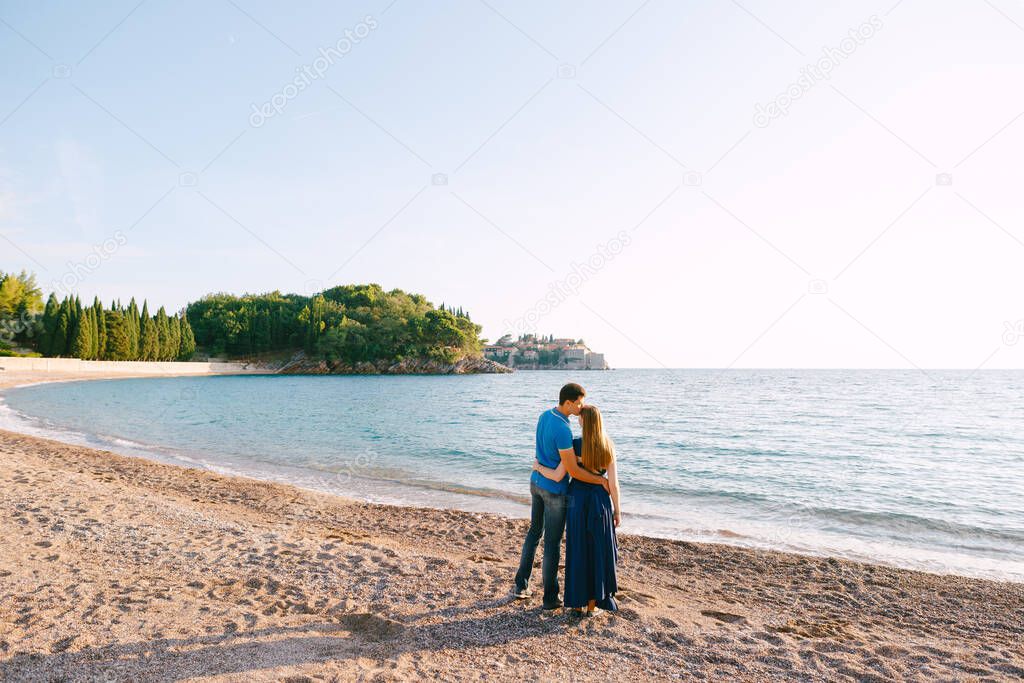 Man kisses woman in a long blue dress against the backdrop of a panorama of the sea and the villa Milocer