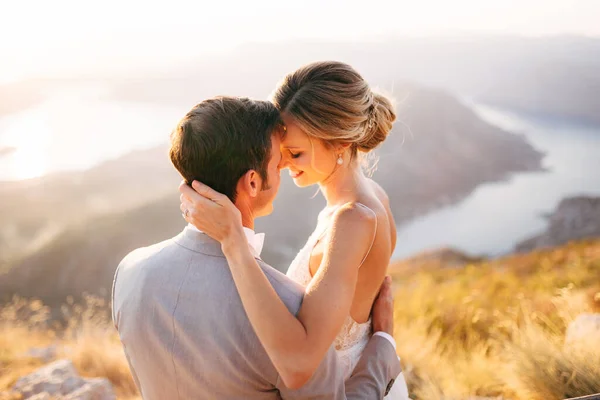 La novia y el novio sentado en la cima del Monte Lovcen con vistas a la bahía de Kotor, sonriendo y abrazando tiernamente, de cerca —  Fotos de Stock