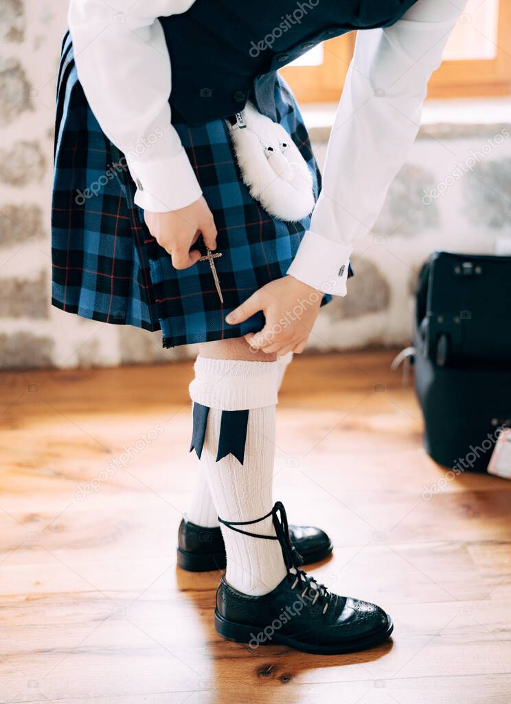 Preparing for a Scottish wedding. Man in high socks, sporran and shoes with long laces attaches a small sword to the kilt