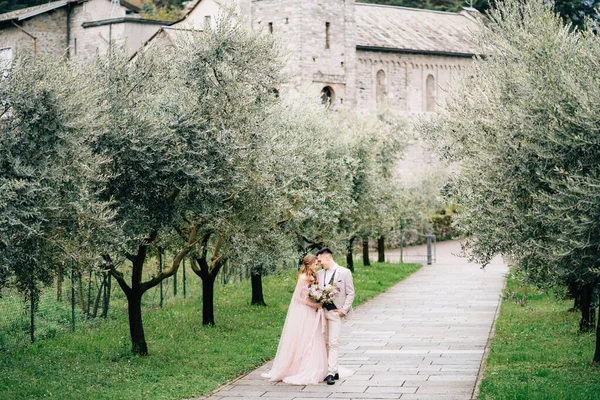 Los recién casados se encuentran en un sendero en un olivar floreciente sobre el fondo de un antiguo edificio en el Lago de Como —  Fotos de Stock
