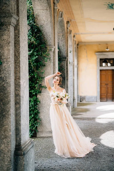Novia en un hermoso vestido con un ramo de flores de color rosa se encuentra en la sala abovedada con la mano en la frente. Lago de Como, Italia —  Fotos de Stock
