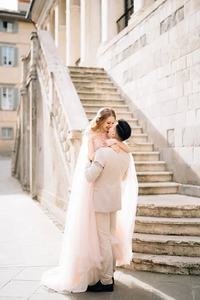 Groom tient la mariée dans ses bras près des marches d'un vieux bâtiment à Bergame, en Italie — Photo