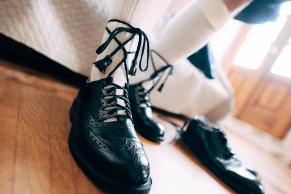 A preparar-se para um casamento escocês. Homem de kilt, meias altas e sapatos com atacadores compridos. Perto um par de sapatos pretos — Fotografia de Stock