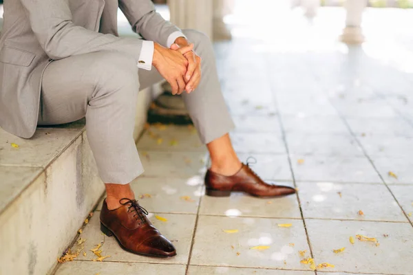 Чоловік у сірому костюмі і шкіряне коричневе взуття сидить на сходинці зі складеними руками — стокове фото