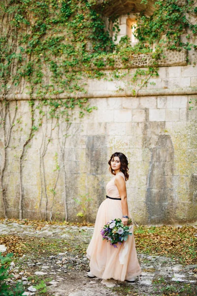 Gyönyörű menyasszony pasztell ruhában sétál egy fényűző csokor virággal a falon — Stock Fotó