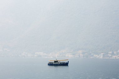 Sis içindeki evlerin ve dağların arka planına vuran sarı güneşli mavi bir tekne..