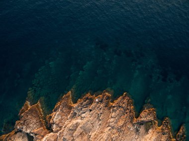 Gelin ve damat kayalık bir sahilde uzanmış, önlerinde derin mavi bir deniz var. 