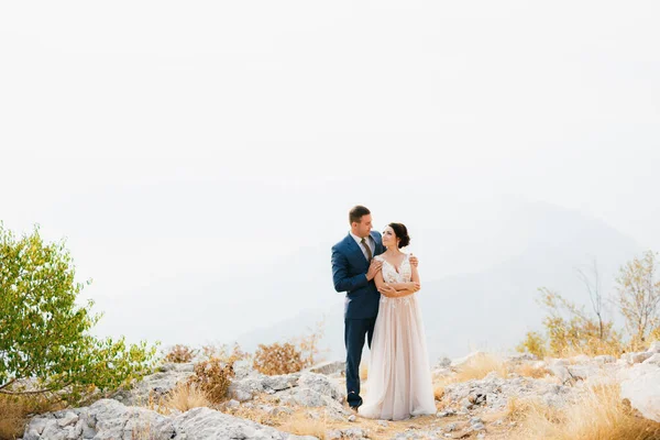 Les mariés se tiennent debout dans les montagnes, le marié étreint doucement la mariée par les épaules, — Photo