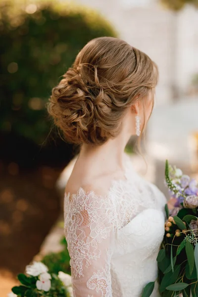 Una sposa con una bella acconciatura in un abito di pizzo stand con un bouquet e guarda di lato, primo piano — Foto Stock