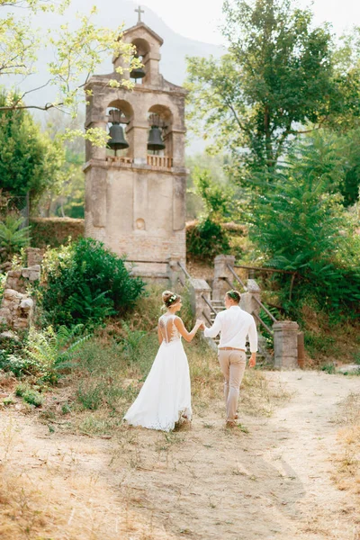 Menyasszony és vőlegény séta az ősi harangtorony közelében a templom Prcanj fogja egymás kezét — Stock Fotó