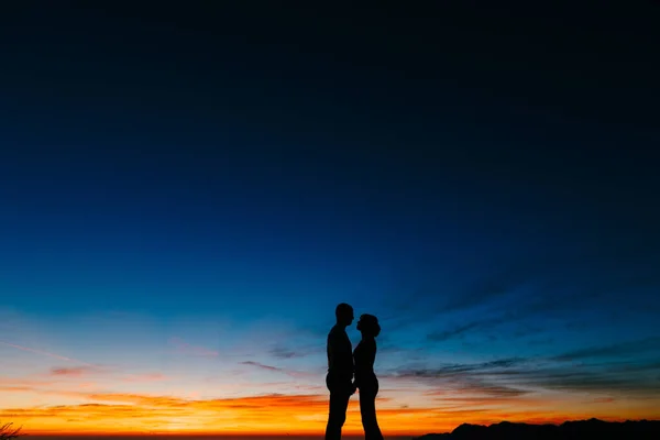 Silhouette di una coppia che si tiene per mano sullo sfondo del tramonto in montagna — Foto Stock