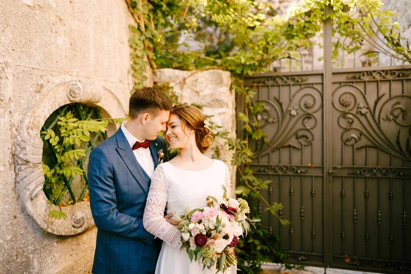Novia sonriente y novio abrazándose en el fondo de puertas de hierro forjado en el jardín — Foto de Stock