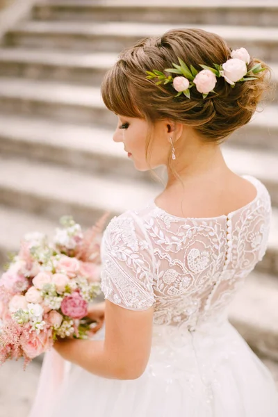 Sposa gentile con un bouquet da sposa tra le mani e fiori tra i capelli in piedi sulle antiche scale del tempio di Prcanj — Foto Stock
