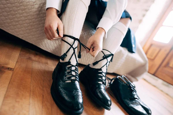 Підготовка до шотландського весілля. Чоловік у кілті і високі шкарпетки сидять на ліжку, зав'язуючи довгі черевики на його черевиках. Поруч лежить пара чорних туфель. — стокове фото