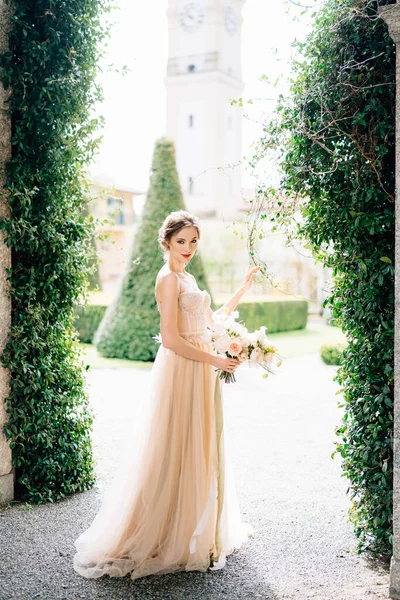 Leende brud i en klänning med en bukett blommor mot bakgrund av gamla byggnader och en trädgård. Comosjön, Italien — Stockfoto